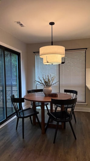 A dining area with a round table, four chairs, a vase with branches, and a hanging light fixture.