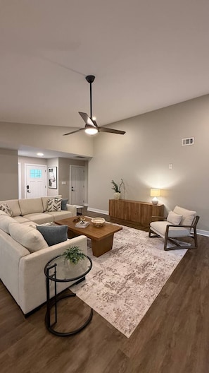 A modern living room with a ceiling fan, a sofa, a coffee table, a side table, and a rug.