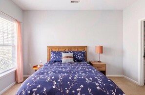 A bedroom with a bed, a nightstand, a lamp, and a window with curtains.