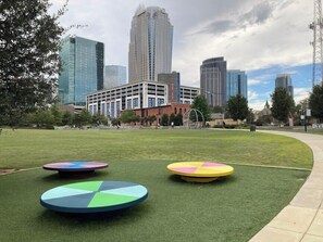 A grassy area with circular objects, a building with a modern design, and a city skyline in the background. - Uptown Charlotte - Best Location in the City (Charlotte)
