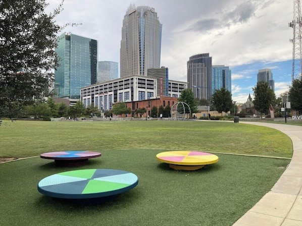 A grassy area with circular objects, a building with a modern design, and a city skyline in the background.