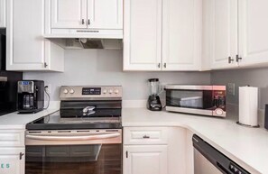 A kitchen with white cabinets, a stove, a microwave, a coffee maker, and a dishwasher.