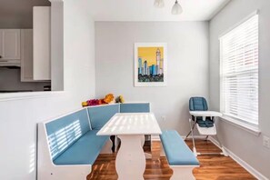 A modern kitchen with white cabinets, a dining area with blue seating, and a cityscape artwork on the wall. - Uptown Charlotte - Best Location in the City (Charlotte)