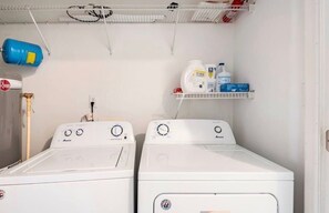 A laundry room with two white front-loading washing machines, a blue gas cylinder, and shelves with cleaning supplies. - Uptown Charlotte - Best Location in the City (Charlotte)