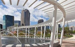 An outdoor area with a water feature, a pergola structure, and modern buildings in the background.