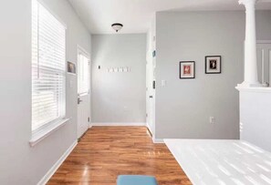 A hallway with wooden flooring, a white door, and a light gray wall with two framed pictures.