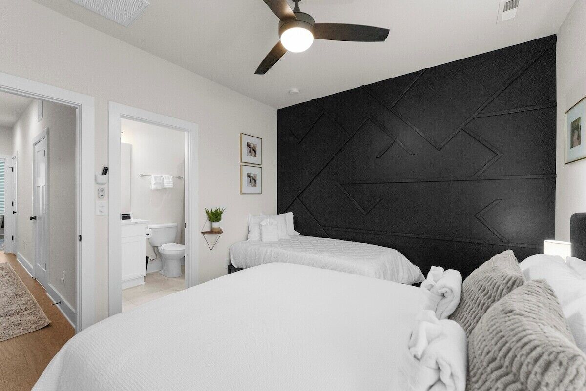 Ein Schlafzimmer mit zwei Betten, einem Deckenventilator, einer Wand in dunkler Farbe und einem sichtbaren Badezimmer mit Toilette und Waschbecken.