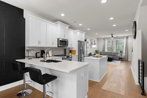 A modern kitchen with white cabinetry, stainless steel appliances, and a central island with bar stools. - South End - Central Charlotte Retreat (Charlotte)