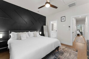 Ein modernes Schlafzimmer mit einem großen Bett, einem Deckenventilator und Blick ins Badezimmer.