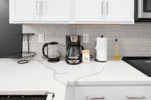 Eine Küche mit weißen Schränken, einer Kaffeemaschine, einer Glas-Kaffeekanne, einer mit 'WINTER BLEND' beschrifteten Kiste und einer Seifenflasche.