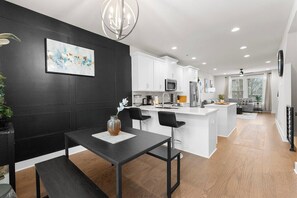 A modern kitchen with white cabinets, a central island, and a dining area with a black table and chairs. - South End - Central Charlotte Retreat (Charlotte)