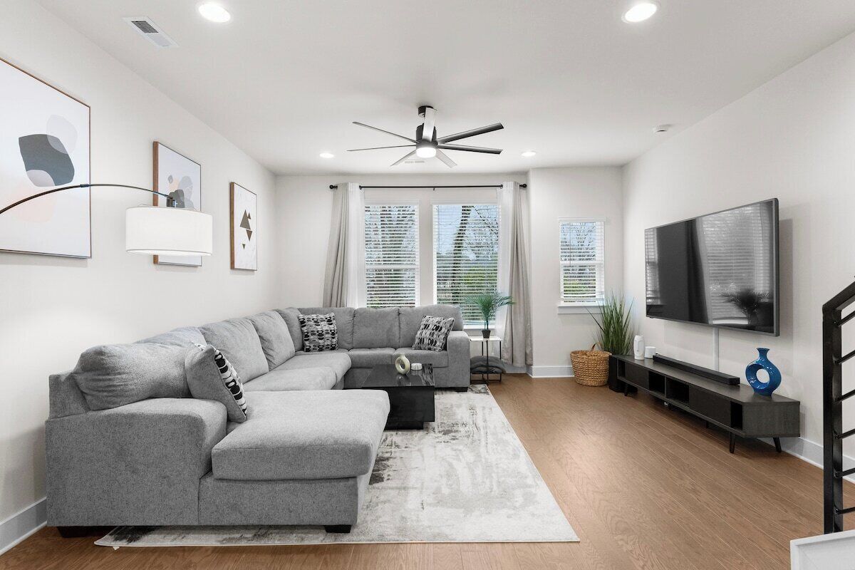 A modern living room with a sectional sofa, a flat-screen TV, and a ceiling fan.