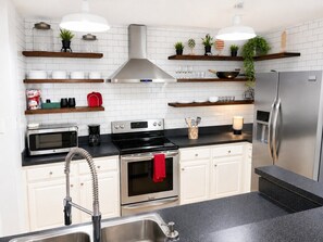 Eine moderne Küche mit weißen Schränken, Edelstahlgeräten und Holzregalen.