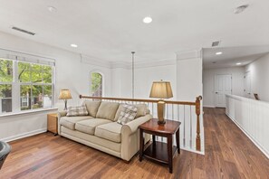 A spacious living room with a wooden floor, a beige sofa, and a lamp on a side table. - Mobility Friendly 3BR + 2 Car Garage & Pool Access (Charlotte)