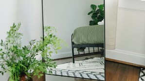 Une pièce avec un grand miroir, un lit recouvert d’une couverture verte, une étagère en bois et un luminaire suspendu.