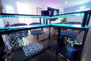 Uma área de bar com balcão, cadeiras e uma televisão.