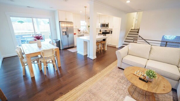 Une cuisine moderne avec des meubles blancs, un îlot central et un coin repas comprenant une table et des chaises en bois.