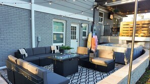 Une terrasse extérieure avec un canapé d’angle, une table basse en verre et un petit foyer.