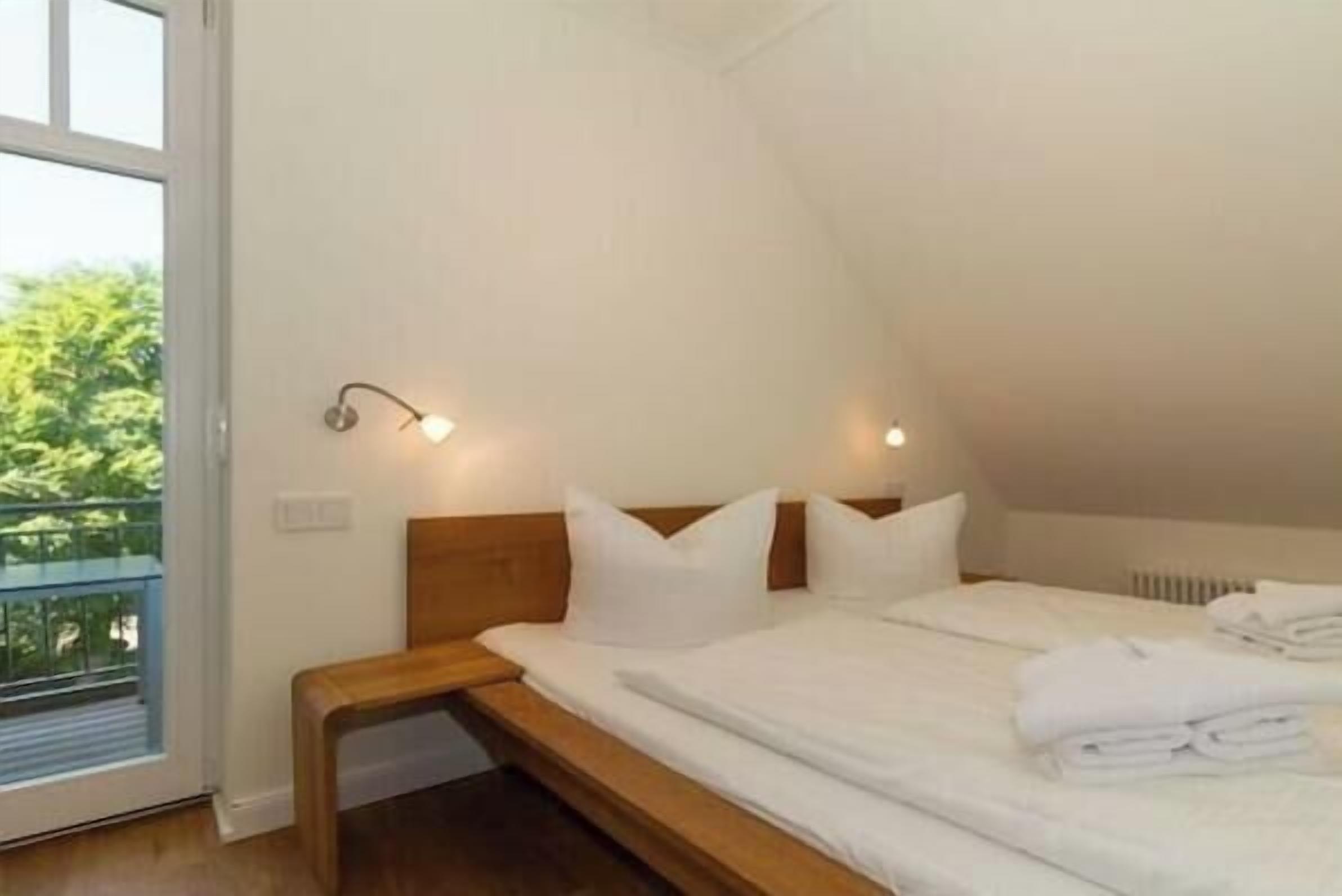 A bedroom with a bed, bedside lamps, and a view of greenery outside.