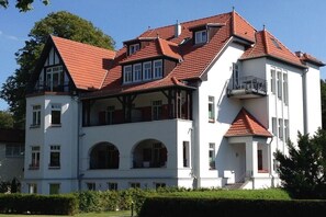 A large, multi-story building with a prominent red-tiled roof, multiple balconies, and a symmetrical facade. - Holiday apartment Villa Löwenstein 319578 (Kühlungsborn)