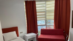 A hotel room with a bed, a red sofa, a small white table, and a window with curtains. - BATIN OTEL (Karabük)