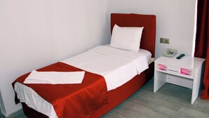 A single bed with a red headboard and white bedding, a bedside table with a phone and a small drawer, and a plain wall with a curtain. - BATIN OTEL (Karabük)