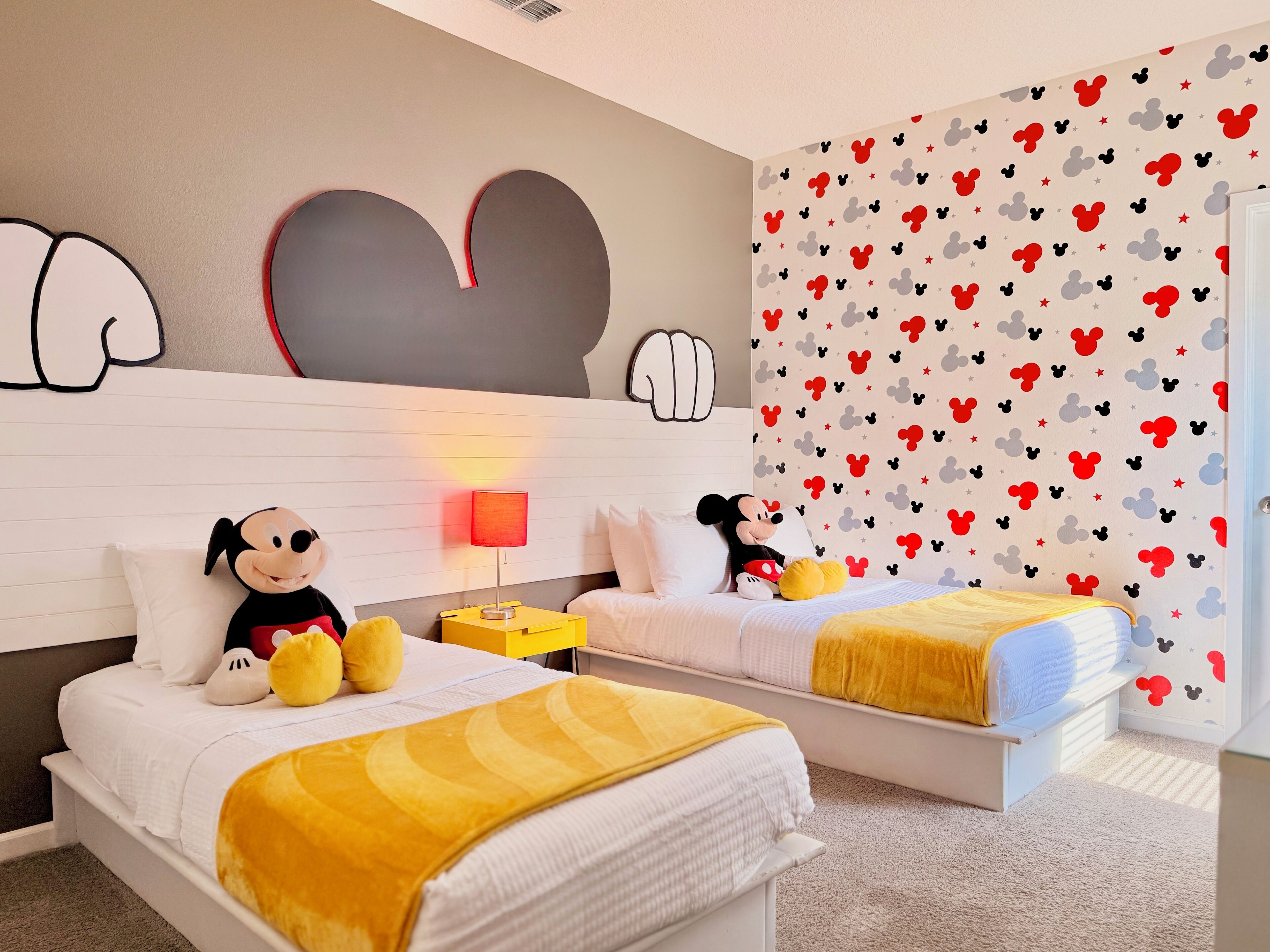Un dormitorio con dos camas, un peluche de Mickey Mouse y una pared temática de Mickey Mouse.