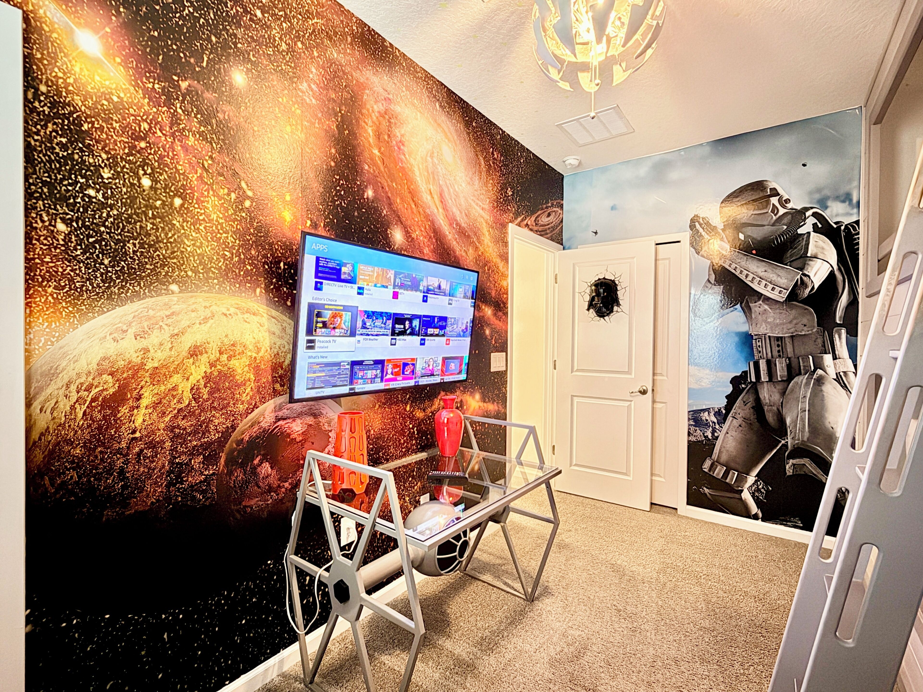 A room with a space-themed mural, a mounted television displaying apps, and a door with a starship decal.
