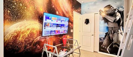 A room with a space-themed mural, a mounted television displaying apps, and a door with a starship decal.