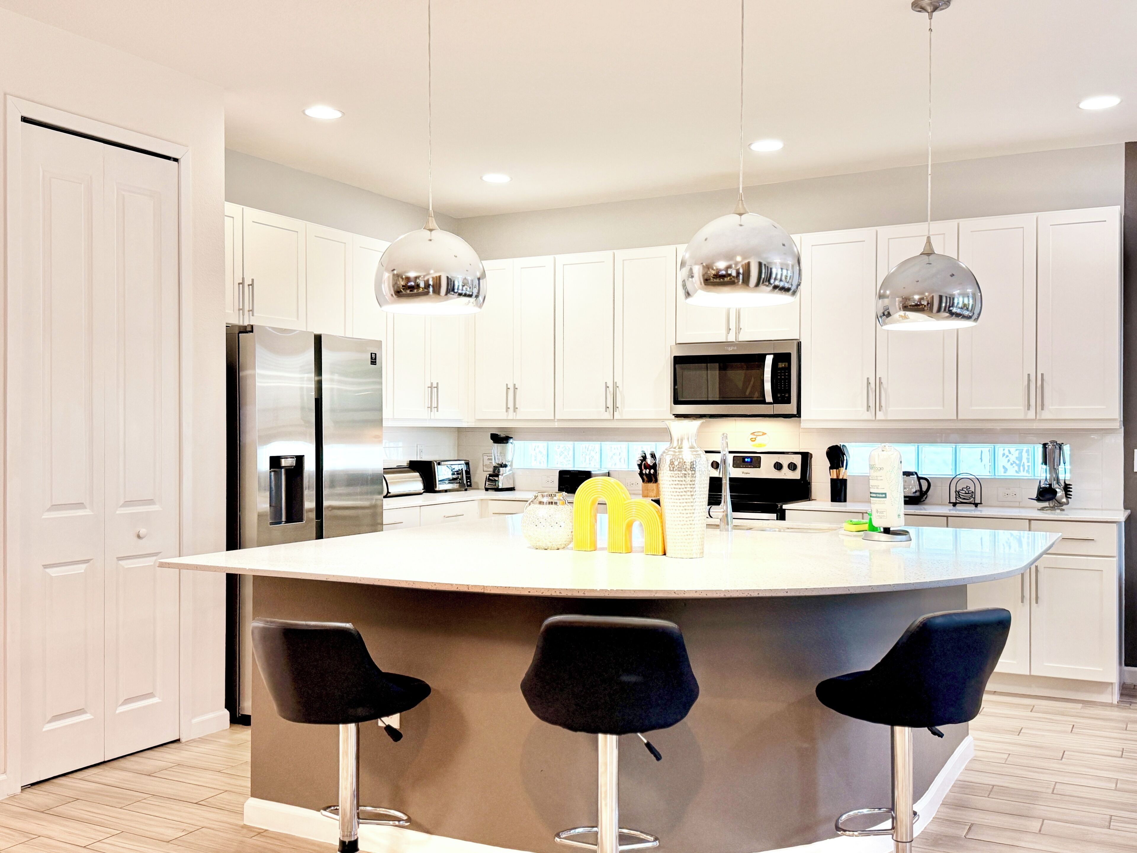 A modern kitchen with white cabinets, stainless steel appliances, and three black bar stools.