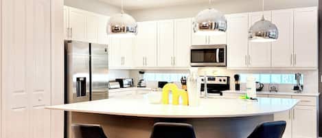 A modern kitchen with white cabinets, stainless steel appliances, and three black bar stools.