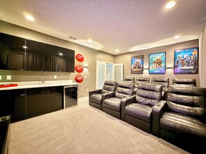 A home theater room with a flat-screen TV, reclining chairs, a popcorn machine, and movie posters on the wall. - Sonoma Resort, 6 Suites, Prime Location, Private Pool, Cinema & Games (Kissimmee)