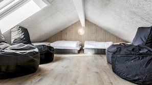 Ein Schlafzimmer im Loft-Stil mit geneigter Decke, Holzwänden und einem Dachfenster. Es gibt zwei Betten und zwei Sitzsäcke.