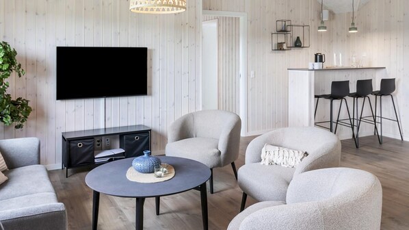 A modern living room with a flat-screen TV, a round coffee table, and two armchairs.