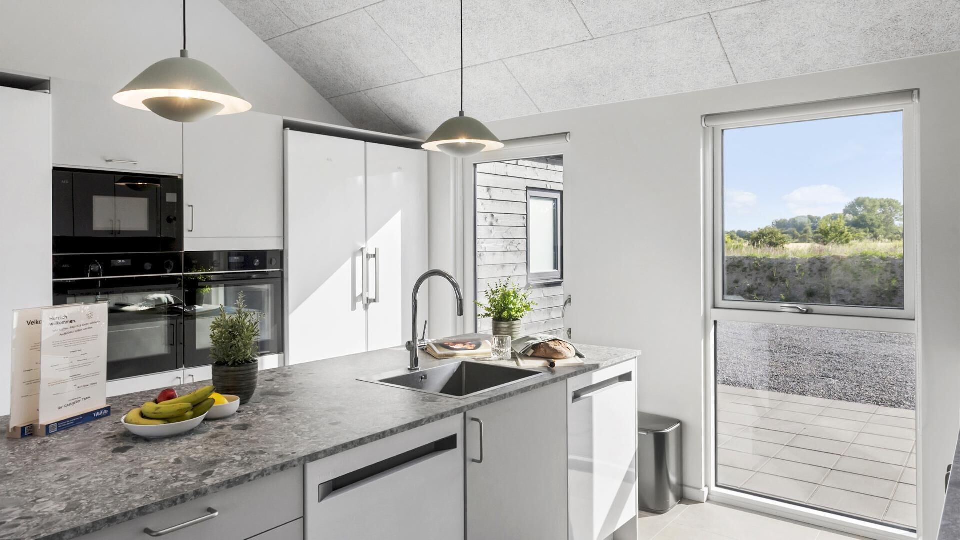 Une cuisine moderne avec des meubles blancs, un évier en acier inoxydable et une fenêtre donnant sur un jardin.