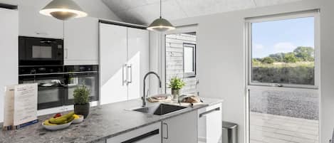 A modern kitchen with white cabinetry, a stainless steel sink, and a window overlooking a garden.