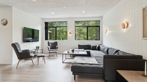 Ein modernes Wohnzimmer mit einem Ecksofa, einem Couchtisch und einem an der Wand montierten Fernseher.