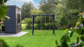 A modern wooden structure adjacent to a swing set in a well-maintained grassy area. - VillaVilla 1002 - Fjellerup, Østjylland (Glesborg)