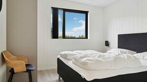 Ein Schlafzimmer mit einem Bett, einem Sessel, einem Fenster und einer Wandlampe.
