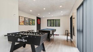 Ein Zimmer mit Kicker-, Billardtisch und gerahmten Bildern an der Wand.