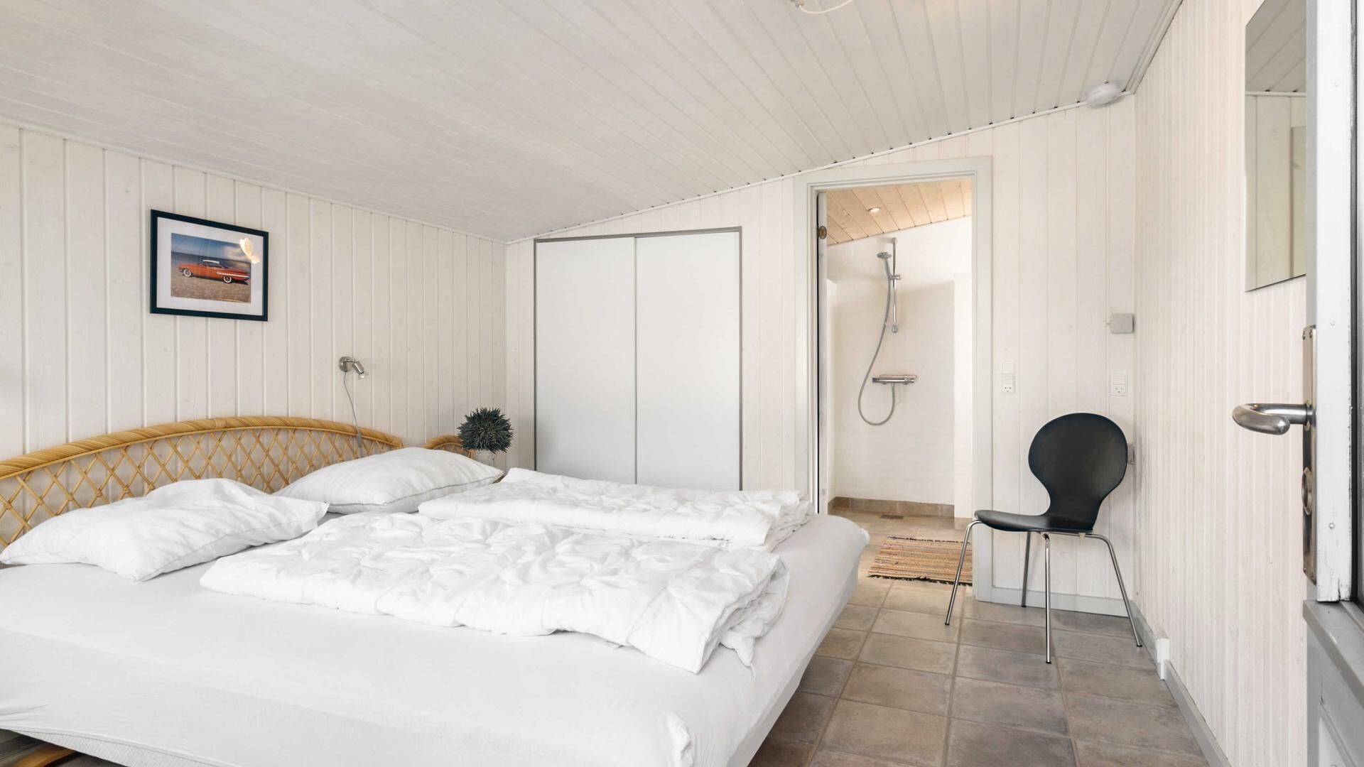 A bedroom with a bed, a chair, a door leading to a shower, and a framed picture on the wall.