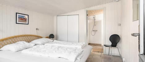 Un dormitorio con una cama, una silla, una puerta que da a una ducha y un cuadro en la pared.
