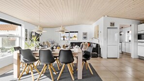 Eine moderne Küche mit weißen Schränken, einem eingebauten Backofen und einem Essbereich mit einem Holztisch und schwarzen Stühlen.
