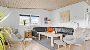 En moderne stue med en sort lædersofa, grå lænestole, et træsofabord og et stort vindue med udsigt.