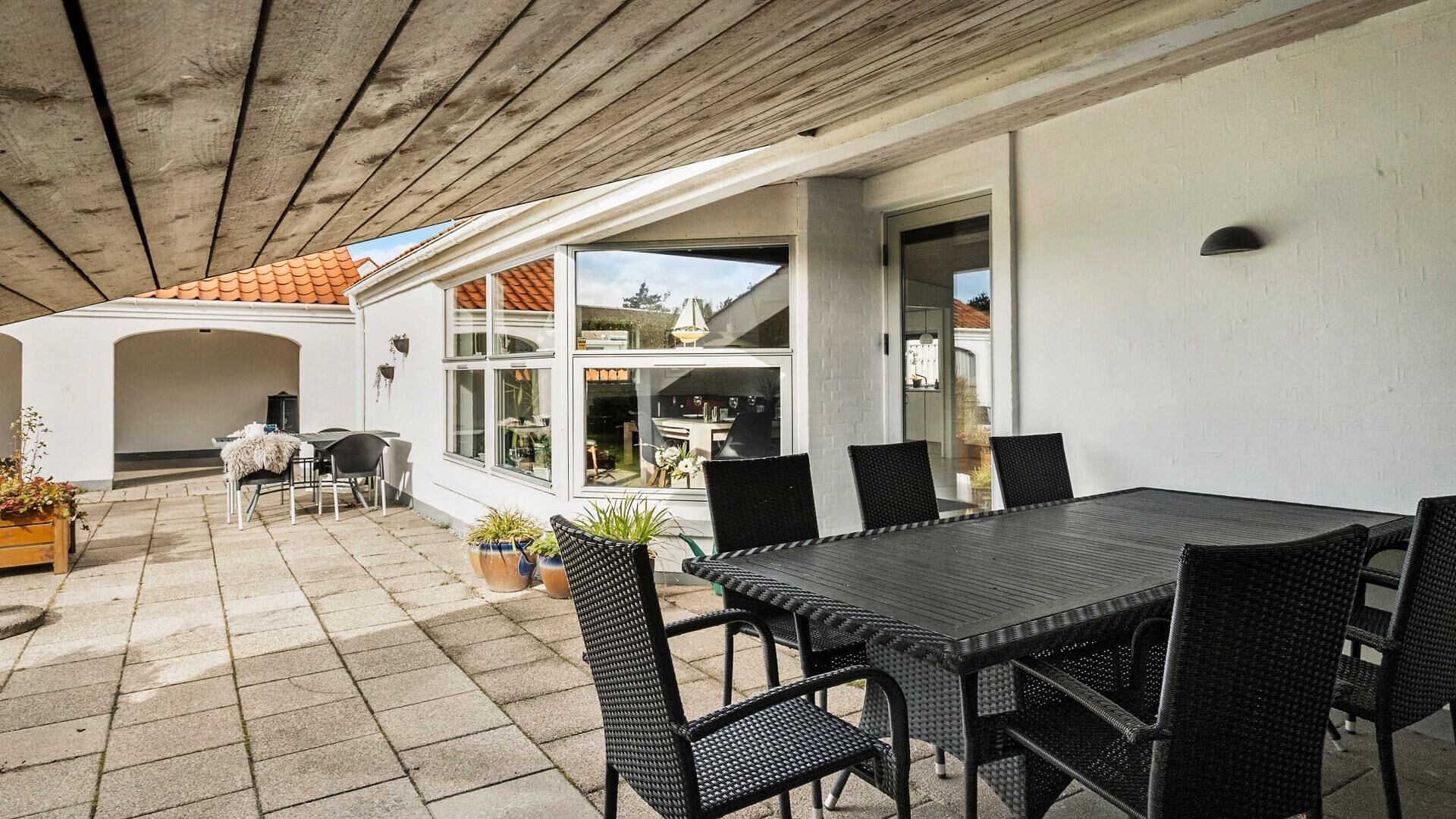 An outdoor patio with a table and chairs, a covered area, and a view of a house.