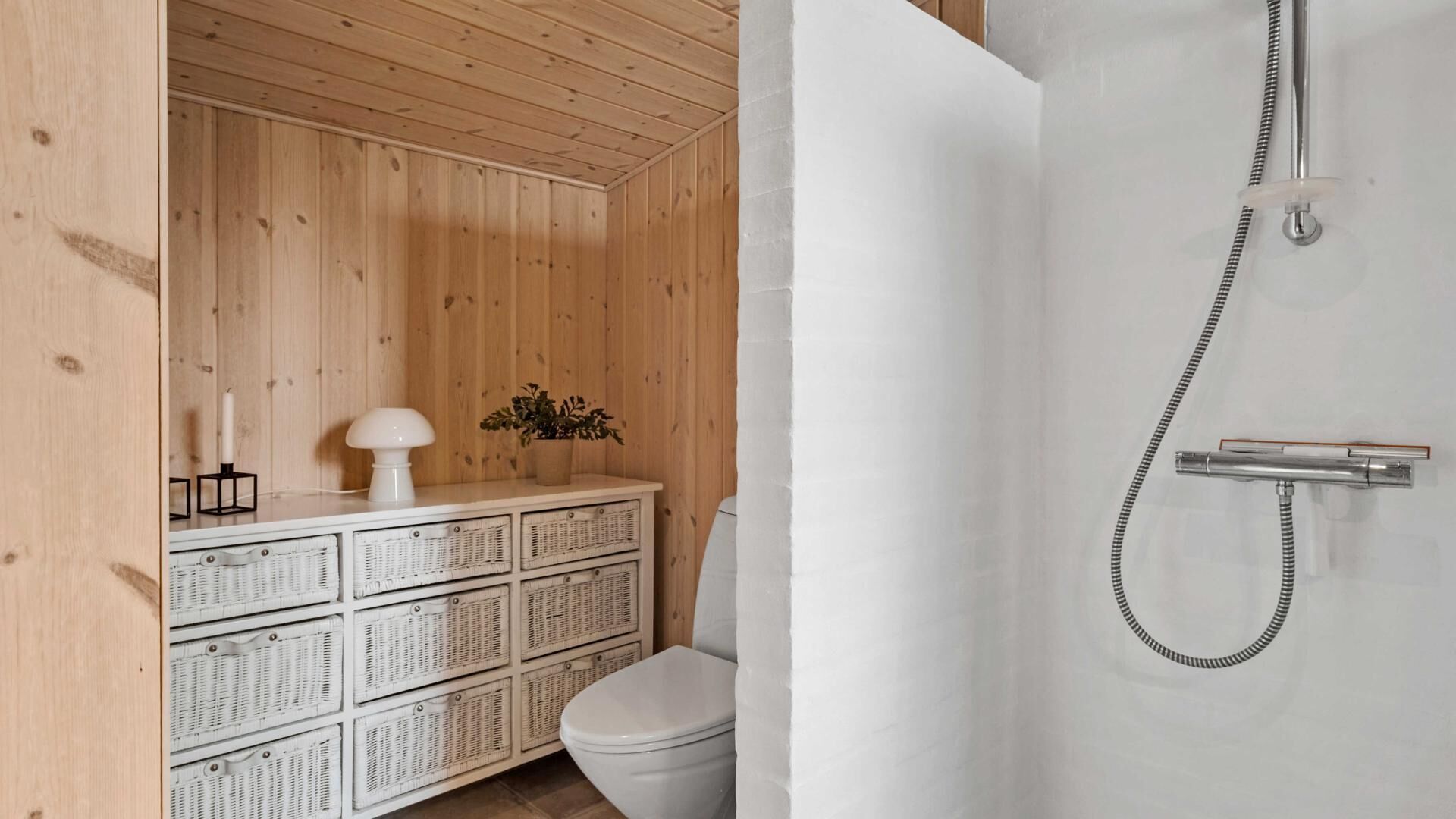 Une salle de bain au décor intérieur en bois, avec des toilettes blanches, des paniers en osier, un rideau de douche blanc et une pomme de douche.