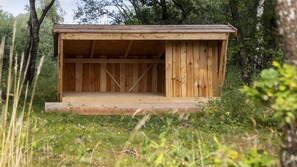A wooden structure with a sloped roof, surrounded by greenery.