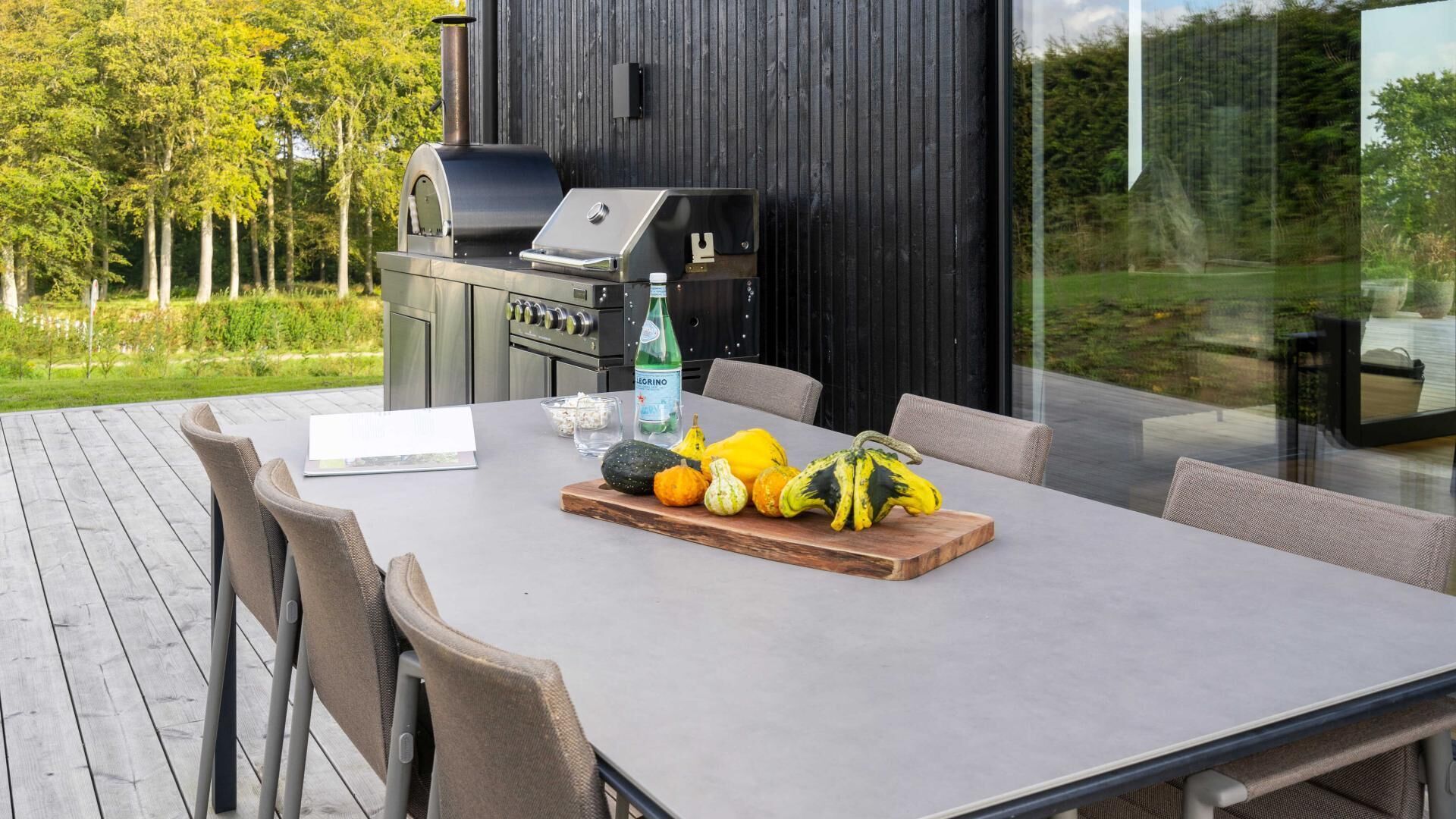 Un espacio para comer al aire libre con mesa, sillas, una parrilla y una variedad de verduras.