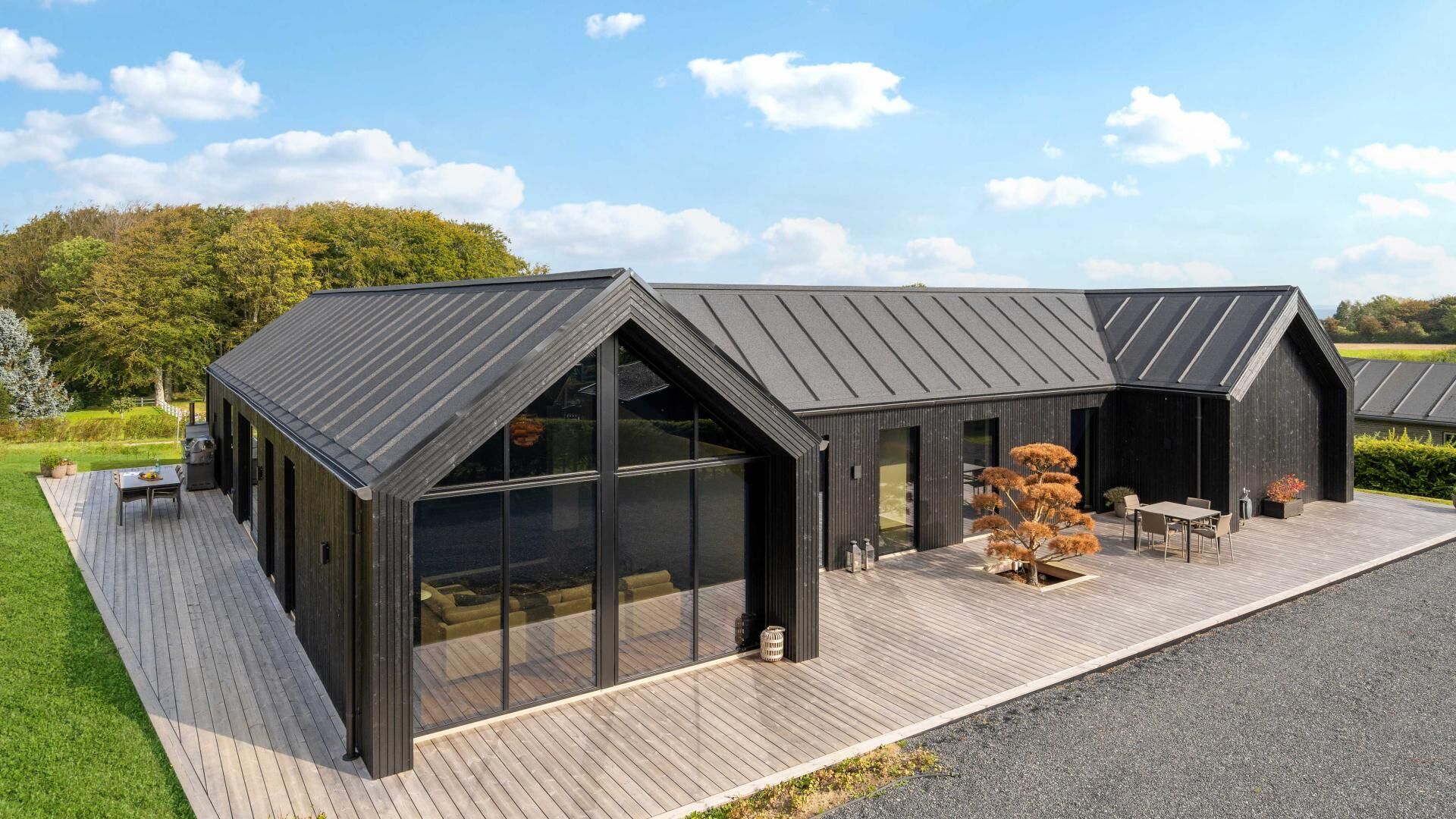 Un bâtiment moderne doté de grandes fenêtres en verre, d’une terrasse en bois et d’un toit en métal.