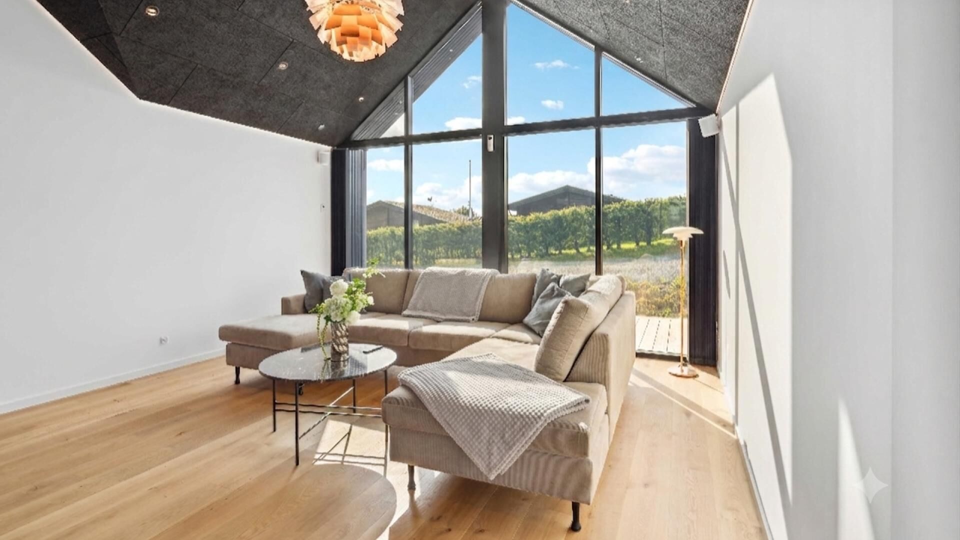 Una sala moderna con un sofá seccional grande, una mesa de centro redonda y vistas a un paisaje montañoso a través de amplios ventanales.